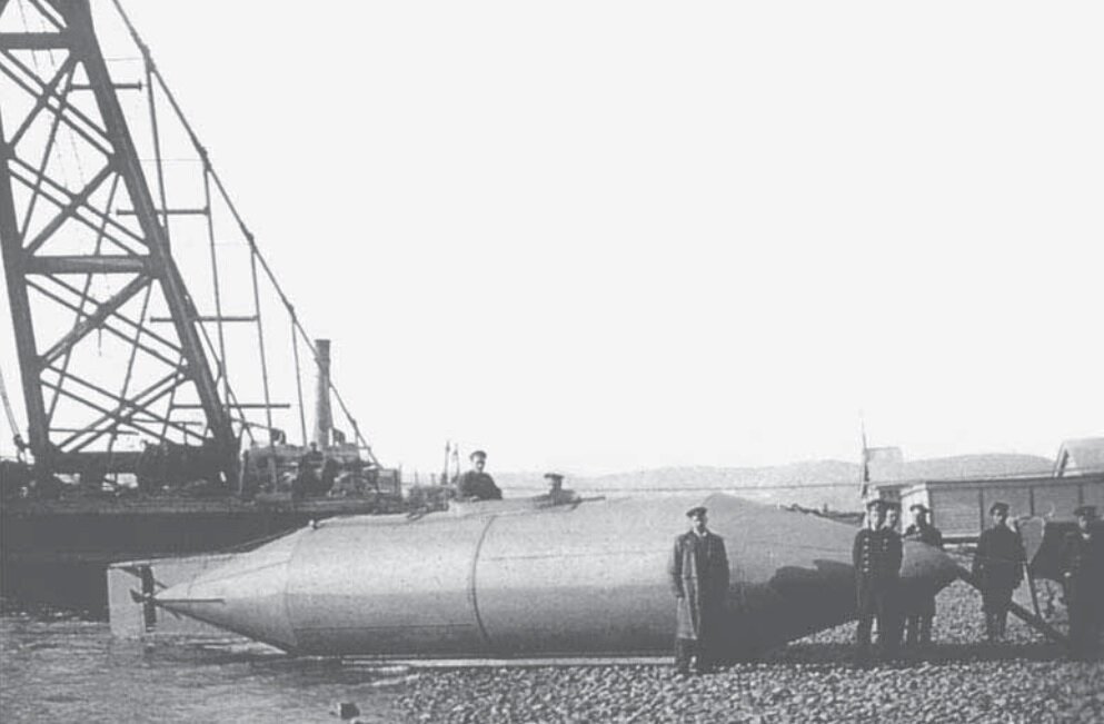 Группа российских военных инженеров и морских офицеров фотографируется возле подводного минного заградителя, созданного по проекту Михаила Налетова, перед началом установки на субмарину двигателя. Ляодунский полуостров, Порт-Артур, 25 октября 1904 года.