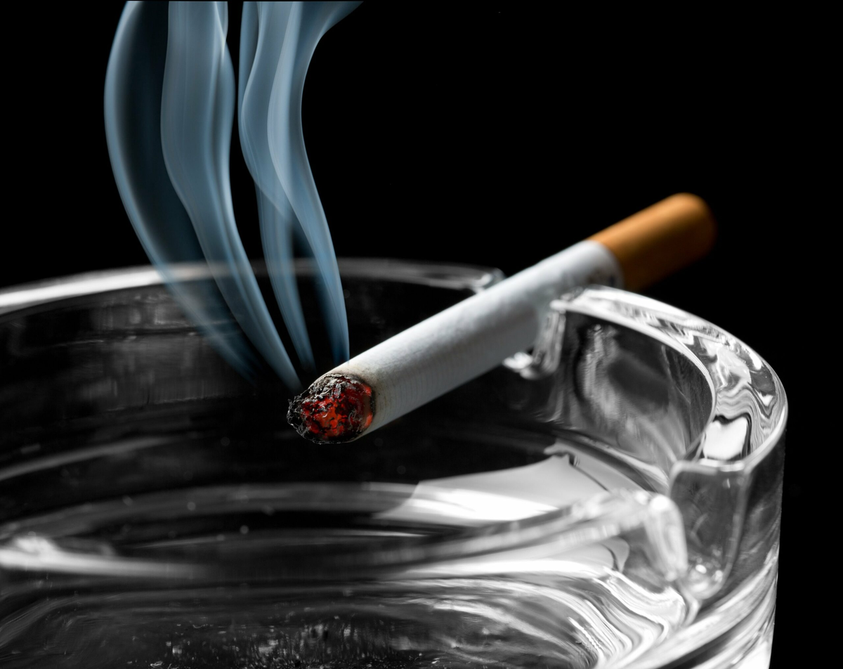 Тлеющая сигарета. Пепельница с сигаретой. Сигарета тлеет. Табачный дым.