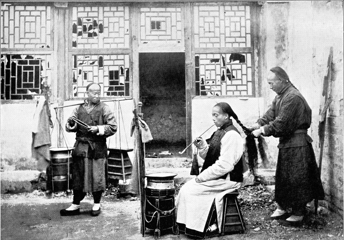 Плетение маньчжурской косы уличными парикмахерами. Пекин, до 1906. (Авторство: Sanshichiro Yamamoto. ‘’Peking‘’ (1906), Общественное достояние, commons.wikimedia)