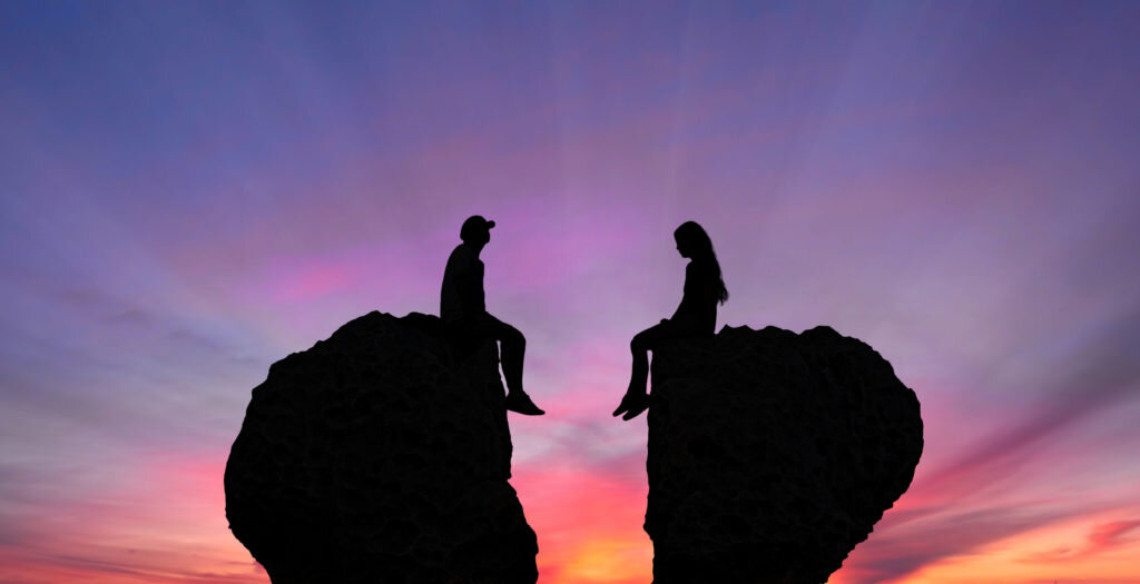 Young couple in quarrel sitting on rocks shaped as broken heart