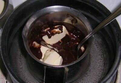     В кастрюльку побольше наливаем воды приблизительно половину объема и ставим на огонь, нам нужна кипящая вода. Тем временем плитку шоколада ломаем в руках насколько можно мелкими кусочками и кладем их во вторую кастрюльку (ту, что поменьше). Сливочное масло натираем на средней терке и добавляем к шоколаду. Лючше всего использовать замороженное, чтобы оно не растаяло в процессе натирания. Как только в кастрюльке закипит вода – помещаем меньшую кастрюльку прямо в кипяток и, постоянно помешивая столовой ложкой или деревянной лопаткой, растапливаем шоколад вместе со сливочным маслом. Важно, чтобы шоколад хорошо смешался с маслом. Как только масса стала однородной - выключаем огонь.   