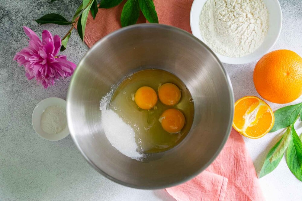 1. В глубокой посуде смешайте 3 куриных яйца и сахар. С помощью миксера взбейте ингредиенты на протяжении 10 минут до получения пышной и светлой массы.