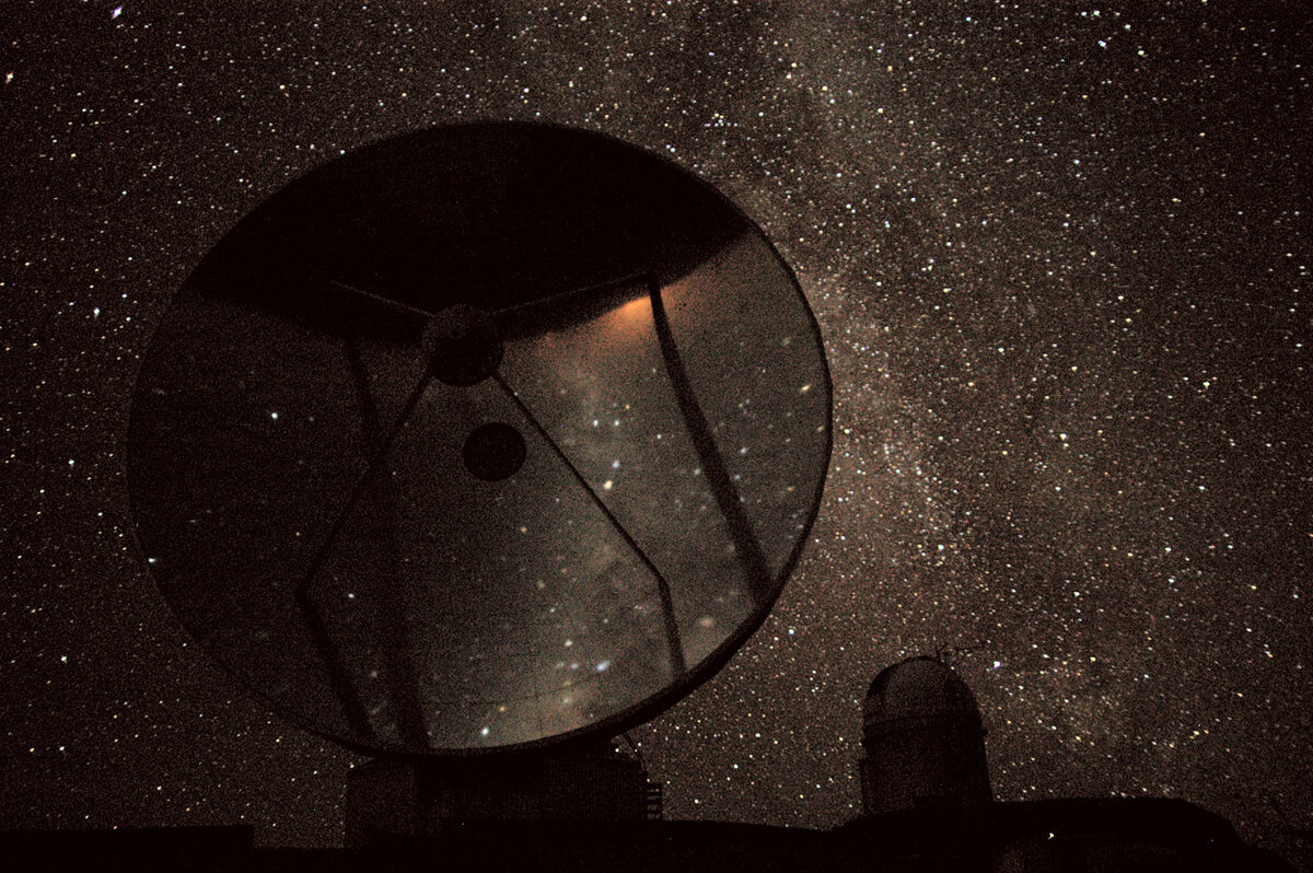 Слева находится разрушенная 15-метровая тарелка шведского субмиллиметрового телескопа ESO (SEST), а справа на заднем плане - купол 3,6-метрового телескопа ESO в самой высокой точке горы. Южный Млечный Путь виден вдоль правой границы SEST и над 3,6-метровым телескопом. За полированной антенной тарелкой SEST виден горизонт и зеркальное отражение позади фотографа. Nico Housen/ESO
