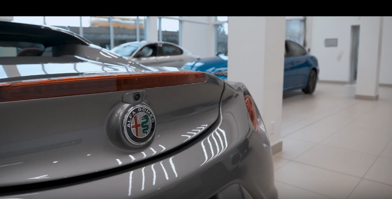 Видно дизайн задней части багажника и брендового знака Alfa Romeo. Над значком есть встроенная камера заднего обзора.