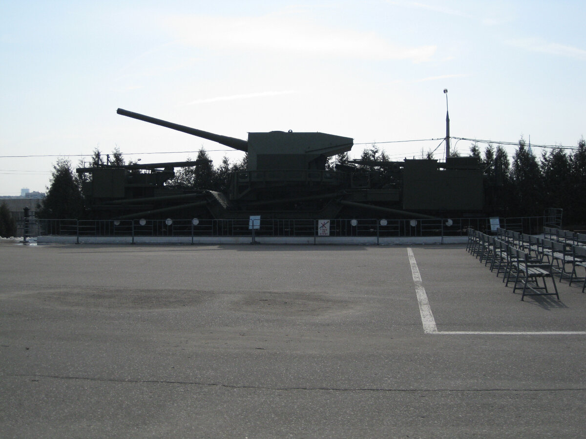 Пушка и вращающаяся открытая башня специфической формы хорошо выделяются на фоне утреннего неба. Заодно можно оценить размеры установки относительно подрастающих ёлочек. Фото автора.