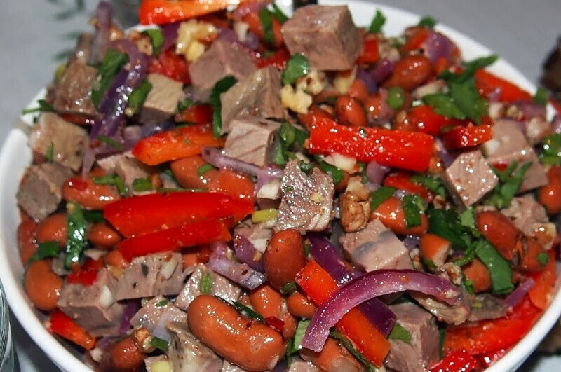  Продукты:

Фасоль (красная, консервированная) — 200 Грамм
Мясо (говядина, баранина или свинина) — 200 Грамм
Лук красный — 1 Штука
Перец болгарский (красный) — 1 Штука
Перец чили (красный) — 1 Штука (по желанию)
Чеснок — 2 Зубчика
Кинза (свежая) — 50 Грамм
Грецкие орехи — 50 Грамм
Соль — - По вкусу
Специи — - По вкусу
Винный уксус — - По вкусу
Растительное масло — - По вкусу

Приготовление:

Открываем фасоль, сливаем воду и затем перекладываем ее в дуршлаг и хорошенько промываем под холодной водой. Выкладываем промытую фасоль на дно глубокой миски.

Чистим красный лук и нарезаем его полукольцами. Слегка сбрызнув лук винным уксусом, перекладываем его к фасоли.

Затем моем красный болгарский перец и перец чили, очищаем их от семян и нарезаем тонкой соломкой. Если кто-то не любит острое, то чили перец можно не использовать, без него тоже получается очень вкусно.

Предварительно отваренное мясо нарезаем соломкой и добавляем в миску к остальным ингредиентам (лучше подождать пока мясо остынет).

Орехи поджариваем на сухой сковороде без добавления масла и нарезаем н небольшие кусочки. Кинзу мелко нарезаем, и все вместе перекладываем в миску. Затем солим и добавляем специи на свой вкус.

Чистим чеснок, мелко его нарезаем или выдавливаем через чесночницу в салат. В конце заправляем наш салат маслом и уксусом и тщательно перемешиваем. Оставляем его на пол часика, чтобы дать настояться и можно ставить на стол.

Приятного аппетита!