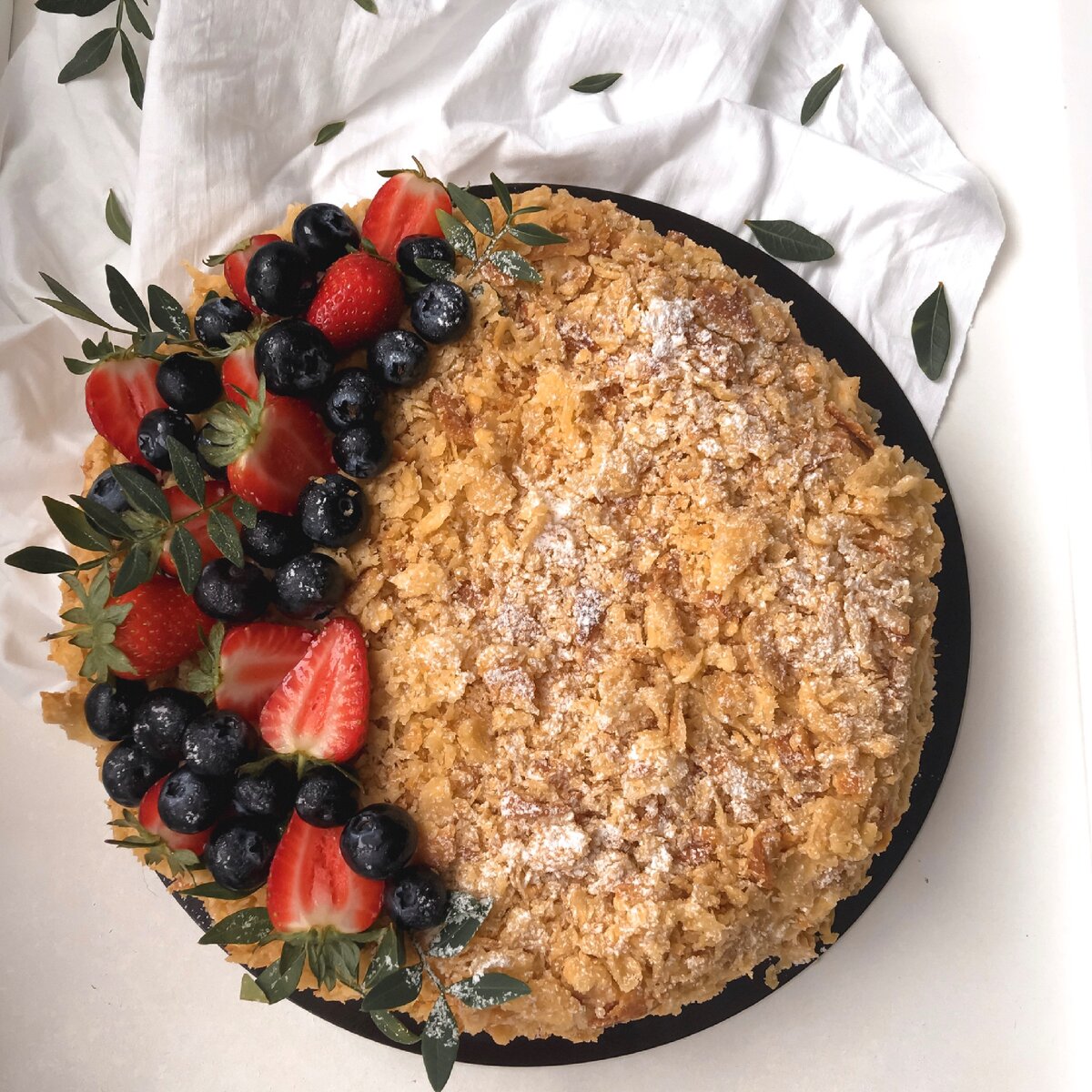 
⠀
Ингредиенты:                                                      ⠀. Мука - 750 гр.                                               ⠀. Сливочное масло - 600 гр.
⠀. Яйца - 2 шт.
⠀. Соль - 1 ч.л.                                                     ⠀. Уксус 5-7% - 1,5 ст.л.                             ⠀. Вода - 220 мл 
       ⠀ Для крема:                                            ⠀. Молоко - 1 литр                                           ⠀. Сахар - 300 гр.                                              ⠀. Яйца - 4 шт.                                                  ⠀. Мука - 120 гр.                                            ⠀. Сливочное масло - 320 гр.                   ⠀. Ванильный сахар - 15 гр.                            ⠀. Сахарная пудра для посыпки 
⠀
Приготовим тесто
⠀
⠀В емкость  разбиваем 2 яйца, добавляем 1 ч.л соли, 1,5 ст.л 5-7% уксуса, перемешиваем. 
⠀
Добавляем, 220 мл ледяной воды,  перемешиваем. Всего должно получиться 375 мл. жидкости. Убираем в холодильник.
⠀
Далее, на рабочую поверхность высыпаем 750 гр. просеянной муки. Всё время окуная замороженное сливочное масло (600 гр) в муку, натираем его на крупной тёрке. Слегка перемешиваем натёртое масло с мукой.
⠀
Масло с мукой собираем горкой, делаем углубление. Достаём  из холодильника нашу жидкость, наливаем в углубление. Быстро замешиваем слоёное тесто. Важно! Тесто не месим, а аккуратно поднимаем тесто с разных сторон к середине, складываем слоями и прижимаем.
⠀
Придаём тесту прямоугольную форму, кладём в целлофановый пакет и отправляем в холодильник на 2-12 часов. Слоеное тесто  готово.
⠀
Для крема: 
⠀
В кастрюлю  наливаем в 1 литр молока, добавляем 320 гр. сахара. Ставим кастрюлю на большой огонь, все время перемешиваем до полного растворения сахара, уменьшаем огонь до среднего и оставляем молоко нагреваться. 
⠀
В другой емкости смешиваем 4 яйца, добавляем 120 гр. муки, перемешиваем до однородности (лучше делать это венчиком).
⠀
В полученную смесь постепенно вливаем горячее молоко, перемешиваем. Далее возвращаем все в кастрюлю. Ставим кастрюлю на огонь и, все время перемешивая венчиком, варим крем до загустения.
⠀
После, снимаем с огня. Добавляем в 20 гр. сливочного масла, перемешиваем. Переливаем крем в миску, накрываем пищевой пленкой и оставляем остывать до комнатной температуры.

Выпекаем коржи. Вынимаем тесто из холодильника. Делим подготовленное тесто на 3 части: две одинаковые побольше и одну поменьше. Я делала торт круглым, выпекая каждый корж отдельно, но вы можете выпекать коржи размером с противень, после чего поделить их пополам, всего у меня получилось 4 коржа и еще один корж меньшего размера для посыпки.
⠀
На стол, присыпанный мукой, кладем кусок теста. Раскатываем тесто толщиной, приблизительно, 3-4 миллиметра, по размеру противня. 
⠀
Выкладываем на противень раскатанное тесто, края слегка прижимаем. 
⠀
Выпекаем  в разогретой духовке  200-220 гр., приблизительно, 20 минут. Для того, чтобы проверить готовность коржа, приподнимаем край коржа - если корж не прогибается, он готов. 
Готовые коржи вынимаем из духовки, даем остыть. Также выпекаем оставшиеся коржи. Корж для посыпки выпекаем на несколько минут дольше.
⠀
После того, как наша масса для крема остыла, приготовим заварной крем. 
⠀
В миску кладем 300 гр. мягкого сливочного масла, взбиваем (масло должно стать белым). Далее, во взбитое масло понемногу добавляем нашу массу для крема каждый раз взбивая в плотную массу. В процессе взбивания добавляем 15 гр. ванильного сахара. Взбиваем до получения пышного крема. Масляный заварной крем и коржи для торта Наполеон готовы.
⠀
Собираем торт. 
⠀
Кладем один корж на доску, выкладываем на него четвертую часть крема, разравниваем. Кладем второй корж гладкой стороной вверх, смазываем его кремом  и так с каждым коржем. Последний, четвертый корж кладем гладкой стороной вверх и смазываем бока и верх торта оставшимся кремом.
⠀
Корж, который мы выпекали для посыпки измельчаем руками в крошку. Добавляем 1 ст. л сахарной пудры, перемешиваем и обсыпаем бока и верх торта крошкой.
⠀
Верх торта дополнительно посыпаем сахарной пудрой. По желанию можно украсить торт ягодами. Я взяла  клубнику, голубику и веточки фисташки. ⠀
Домашний торт Наполеон готов, приятного аппетита! ❤️