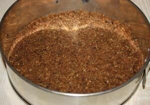    Для начала следует достать из холодильника все молокопродукты и фрукты и позволить им нагрется до комнатной температуры. Далее, берем разъемную форму и выстилаем ее пергаментом для выпечки. Высыпаем туда наше шоколадное печенье и мелко-мелко крошим его (можна сделать это при помощи колотушки или просто перемолоть в блендере). Сорт печенья вы с легкостью можете заменить любым другим, по вкусу, наприме отлично подойдут печенюшки "топленое молоко". 