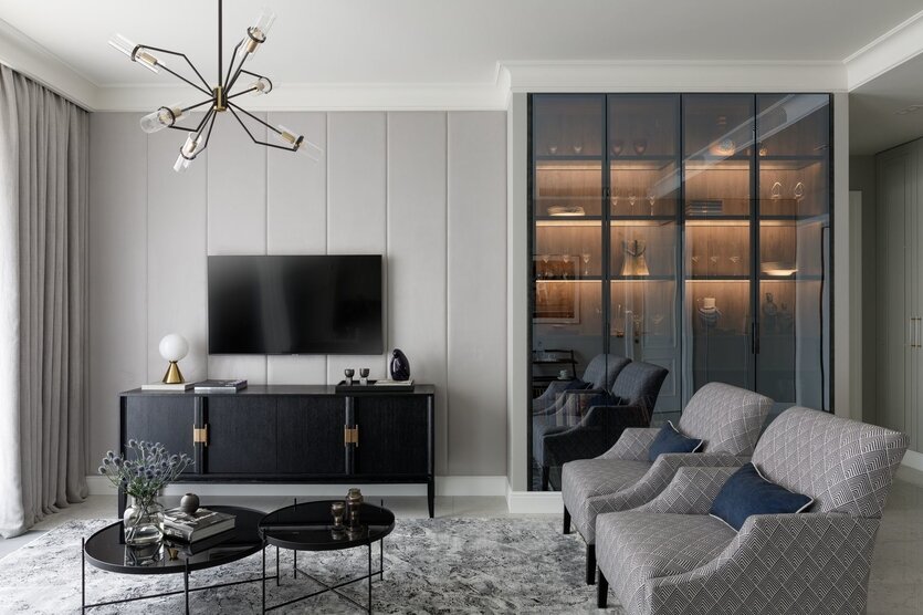 В зоне гостиной дизайнер разместила витрину (Giulia Novars) с тонированными стеклами для хранения книг, коллекции хрусталя и сувениров; в закрытых секциях организовано хранение документов. Диван, Dantone Home. Люстра, Troy lighting. На диване — авторские подушки с вышивкой работы Стаса Лопаткина. Настольная лампа на комоде, Mitzi.