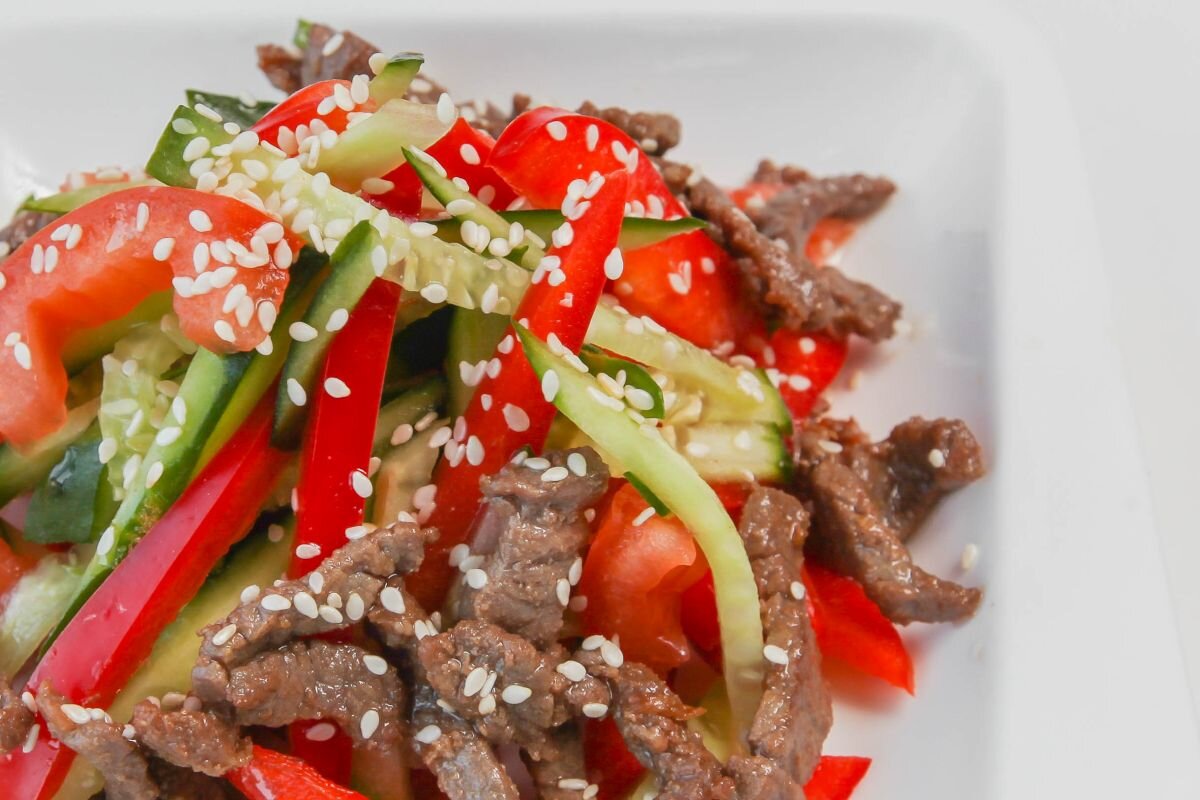 Нарежьте тонкими кружками репчатый лук, помидоры и свежие огурчики. Мясо можно использовать как вареное, так и обжаренное.  Смещайте все ингредиенты, посолив и поперчив по вкусу. Полейте капелькой оливкового масла и украсьте зеленью или кунжутными семенами. 