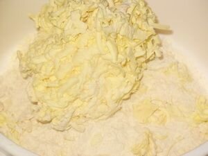     Два стакана просеянной муки высшего сорта засыпаем в миску. Далее уда всыпаются сухие дрожжи. Сливочное масло нужно заранее заморозить в холодильнике для того, чтобы его можно было без проблем натереть. Берем крупную терку и натираем охлажденное масло. Добавляем его в смесь муки и дрожжей и тщательно перемешиваем. Лучше всего для этого подойдет деревянный прибор, например, лопатка. Вбиваем яйца. Далее добавляем в тесто немного сахара, соли. По необходимости можно добавить немного кипяченной или фильтрованной воды. Замешиваем тесто. Если масса получается слишком мягкой нужно добавить муки и продолжать замешивать массу, пока тесто не перестанет приставать к рукам. Оставляем в таком виде тесто в теплом месте на 15 минут. Также его нужно накрыть чистой салфеткой или кухонным полотенцем.   