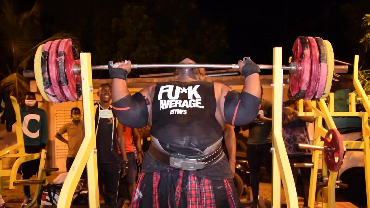 Его стартовое положение в жиме стоя. Видим что жмет с уровня подбородка. Таким образом спортсмен работает и на легких и на средних весах, для него это уже устоявшаяся техника. Также он использует тугие налокотники, а они способны добавить порядка 5-10 кг. Но всё это не отменяет его огромной силы.