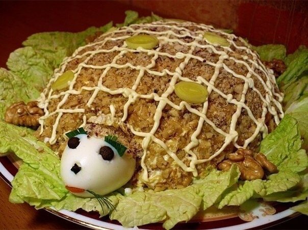 Салат "Черепаха"
Ингредиенты: куриная грудка - 600 гр, яйца куриные - 4 шт, лук репчатый - 1 шт, сыр твердый - 100 гр, чернослив - 100 гр, яблоки - 250 гр, салат зеленый - 6 листиков, орехи грецкие - 100 гр, майонез - 200 гр, соль.
Готовим: Куриное филе отвариваем до готовности (около 20 минут), остужаем и мелко нарезаем. Варим яйца, разделяем на белки и желтки, желтки крошим, белки трём на тёрке. От одного яйца оставляем половинку для "головы черепахи". Нарезаем мелко лук и заливаем кипятком на пару минут, чтобы снять горечь, затем споласкиваем холодной водой. Чернослив промываем и замачиваем, если суховат. На тёрке измельчаем очищенные яблоки и сыр, яблоко сразу же заправляем майонезом, чтобы не темнело, мелко нарезаем чернослив.
На плоское блюдо кладём листья салата. Располагаем с краю яйцо, которое будет головой черепахи. Половину курицы, заправленной майонезом, выкладываем, формируя туловище. Посыпаем курицу луком, смазывать майонезом не нужно. Следующий слой - белок яйца, промазываем майонезом, затем - яблоки. Выкладываем вторую половину курицы, промазываем майонезом, сверху выкладываем слой желтками и также промазываем майонезом. Распределяем по желтку чернослив. Завершаем слоем сыра.
Теперь оформляем "черепашку". Панцирь делаем из поджаренных и по максимуму очищенных от плёнки неизмельчённых грецких орехов, мордочку оформляем с помощью кусочков маслин, вместо глаз можно использовать горошины черного перца, из целых орешков или из долек соленого огурца делаем лапки черепахи.
"Черепаху" можно подавать к столу. Приятного аппетита!
