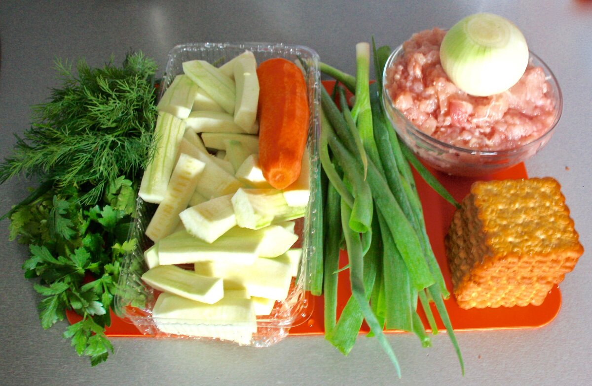 Ингредиенты для ужина, зелень, морковь и кабачок, куриный фарш, репчатый лук и крекеры.