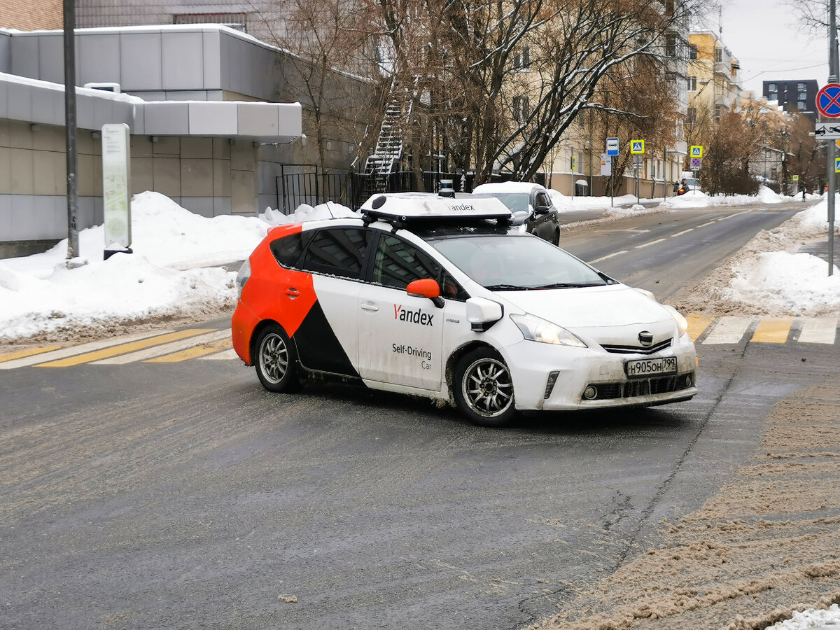 Беспилотный автомобиль Яндекс на базе, кажется, Toyota Prius. Автомобиль сворачивает с улицы Доваторов в Проектируемый проезд № 2309. На фотографии не видно, но человек, сидящий на водительском месте, за руль не держится, автомобиль реально поворачивает сам. 30 января 2022 года.