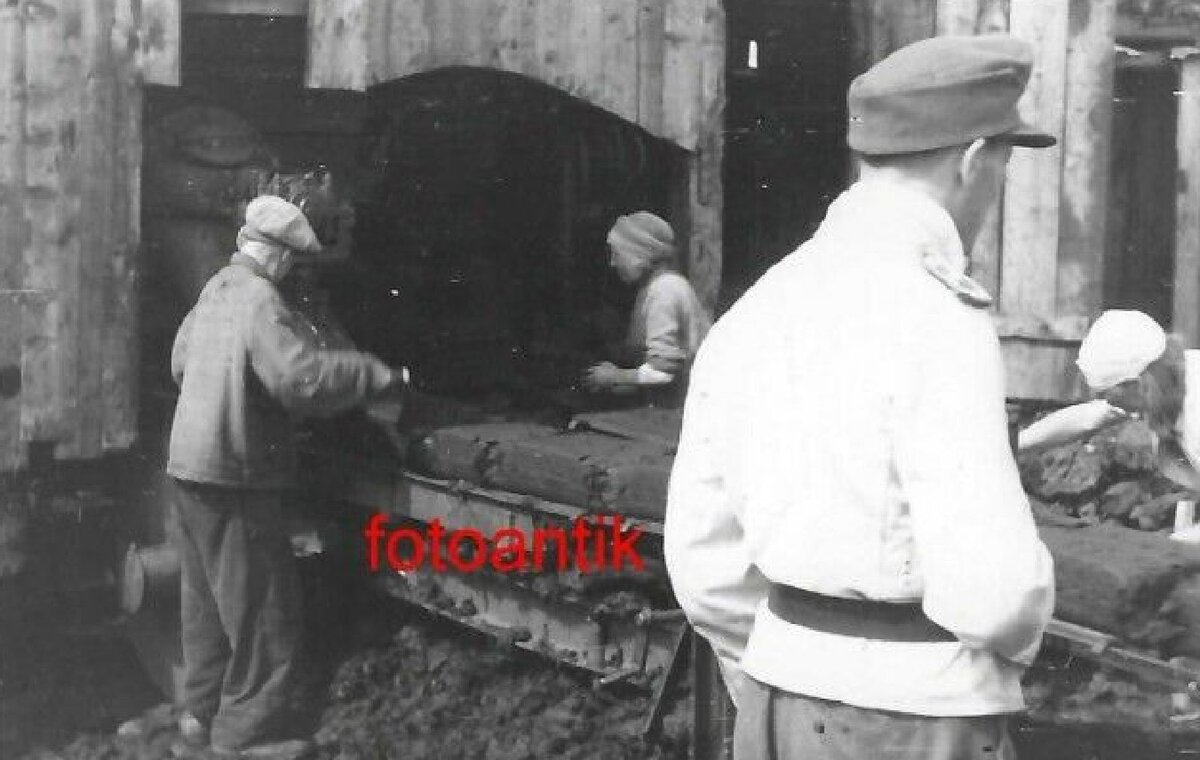 Выход из драги. Видны спрессованные брикеты, которые отправляются на сушку. Кто то из охраны в белом кителе и немецкой старорежимной фуражке. Не знаю кто это, возможно эстонцы. 