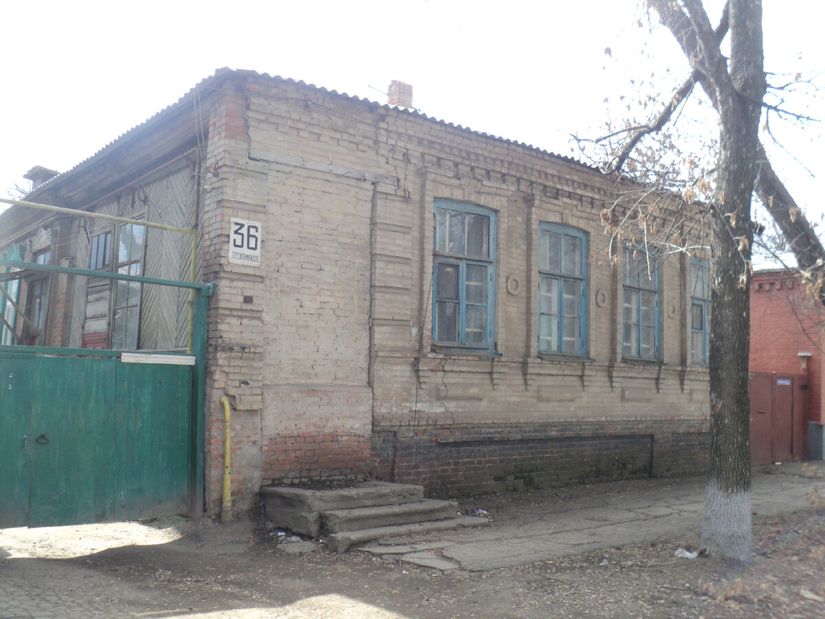 Фото дома где я вырос конца 2000-х годов. Дом неухожен и выглядит не комильфо.  В моё детство и юность он был всегда покрашен - верхняя часть белая или бледно голубая, нижняя - в тёмно серый или чёрный цвет - красили каждую весну маляры из ЖЭКа, краскопультом.  Тротуар перед домом был вымощен каменными плитами, затем сверху положили качественный асфальт. Тут же видно, что асфальт облез, а плиты проступили из под асфальта. Плиты 19 века оказались надежнее асфальта 70-х годов 20 века. Сам же дом был построен в середине 19 века. Они (плиты) вплоне могли помнить и Пушкина, и Лермонтова, и декабристов... Дорога на Кавказ лежала через Каменск, тогда станицу Каменскую на Донце.