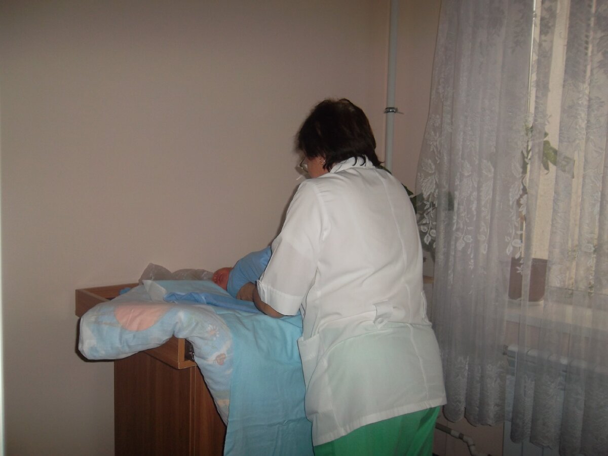 На фото: медсестра заворачивает в одеяло новорожденного.