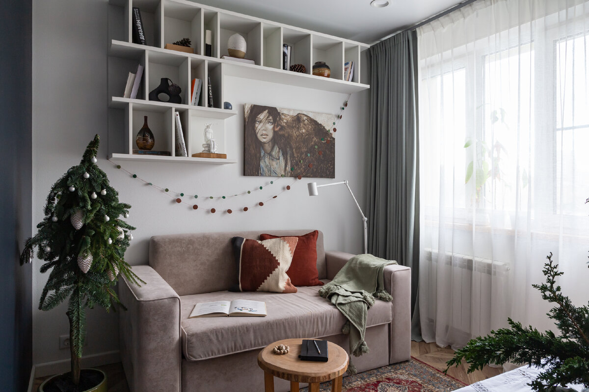 Диван прислонили к стене. Открытые полки над ним используются для хранения книг и декора. Ковёр в этническом стиле на полу поддержали принтом на декоративной подушке.