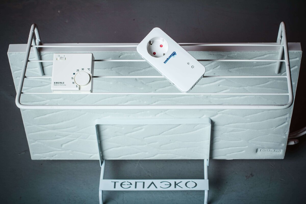 Обогреватель ТеплЭко с сушилкой. На сушилке лежат приборы: GSM розетка и терморегулятор, которые позволят использовать обогреватель наиболее безопасно и энергоэффективно.