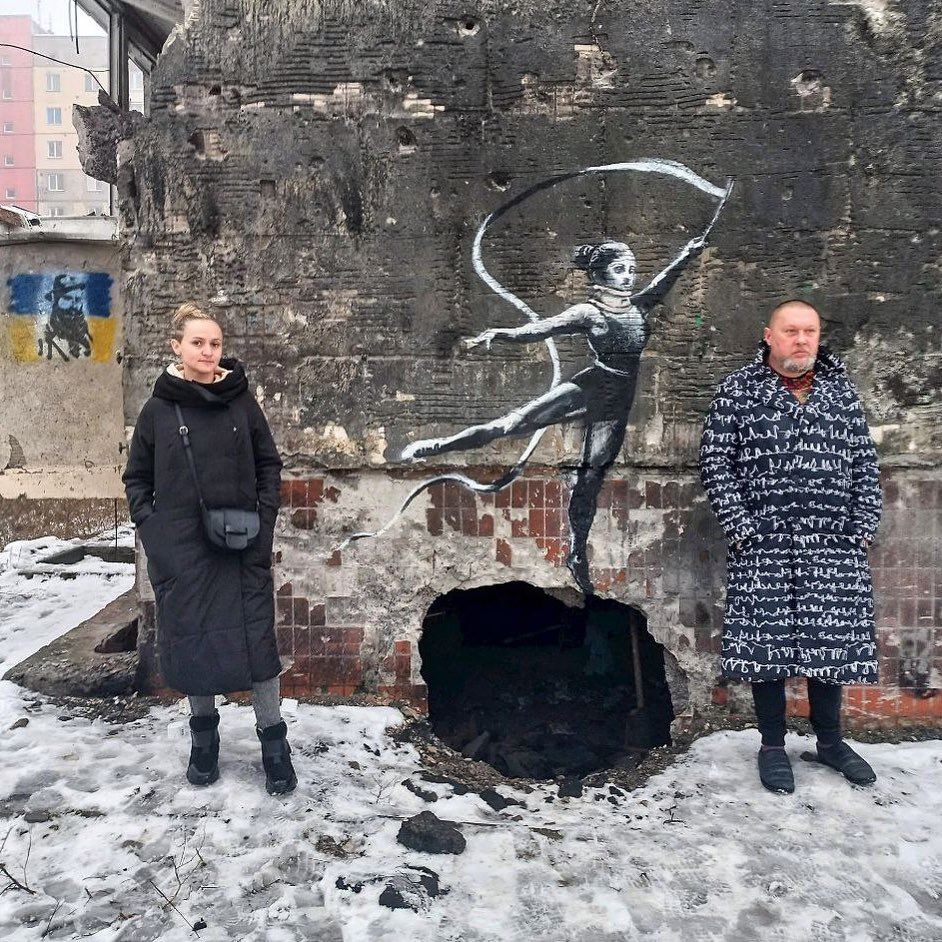 Натуральная девушка похожа на девушку, которая нарисована настене. Можно предположить, что художник создавал гимнастку с лентой опираясь на натуральныйобъект )девушку без ленты).

♦
https://www.facebook.com/doroshenko.kostyantyn/posts/pfbid02QWnVDxBscDRP4fP6iNcFr7QVPNUY2gSD7gNfs5UorDtmjYuxL9GTeQoqgJ5dNx7hl