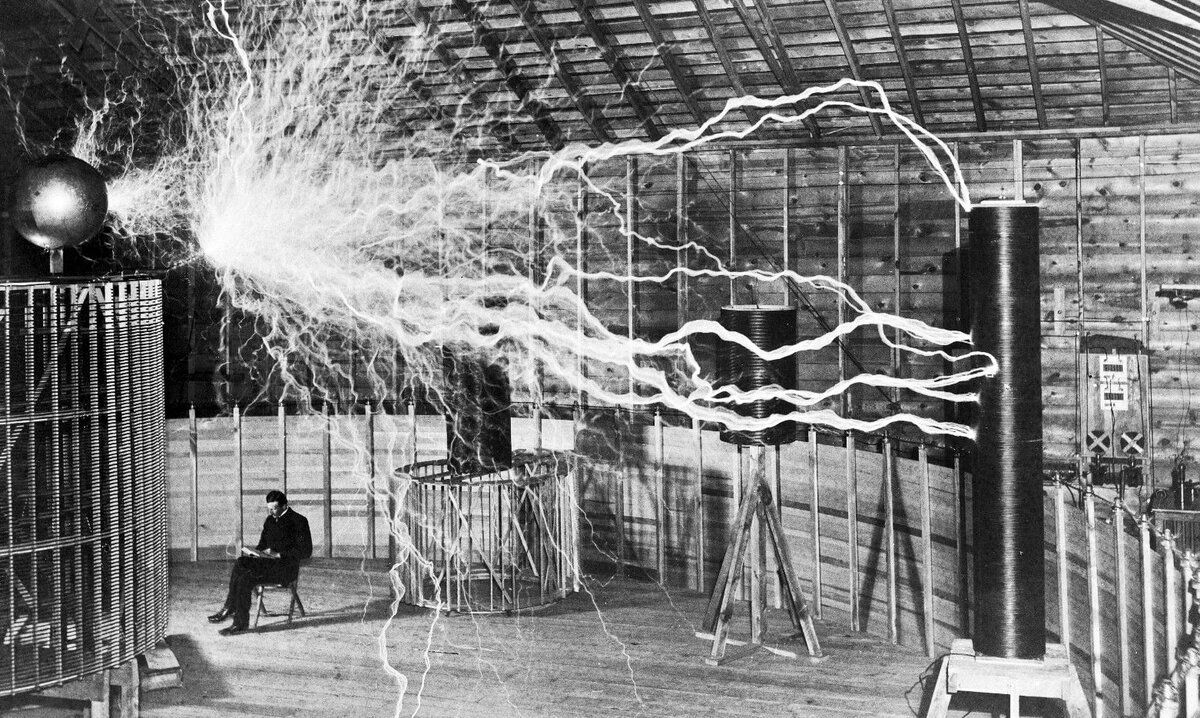 Никола Тесла с книгой «Tеория натуральной философии» перед спиральной катушкой его высокочастотного трансформатора в лаборатории, 1896 г.