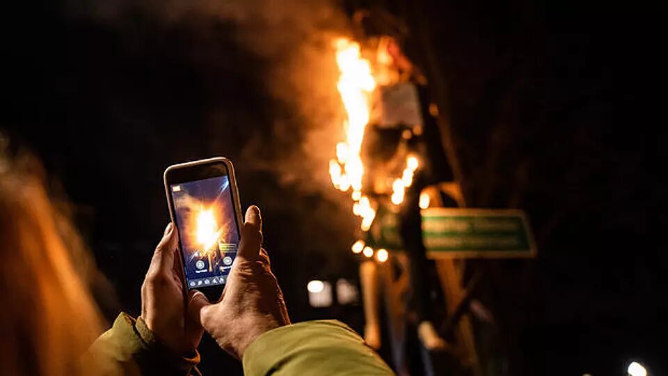 Любопытствующие снимают костёр на телефоны.https://www.tv2lorry.dk/tv2dk/dukke-af-mette-frederiksen-med-truende-besked-braendt-af-under-demonstration