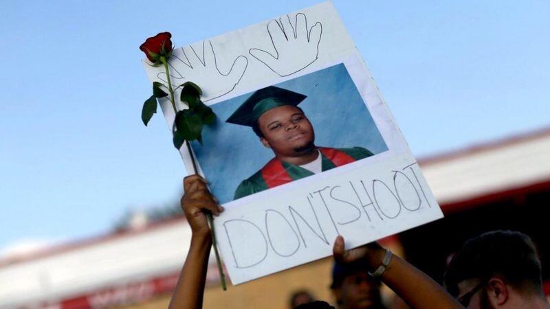 Участник демонстрации держит над головой портрет 18-летнего Майкла Брауна, застреленного в 2014 году в городе Фергюсон, штат Миссури, полицейским.