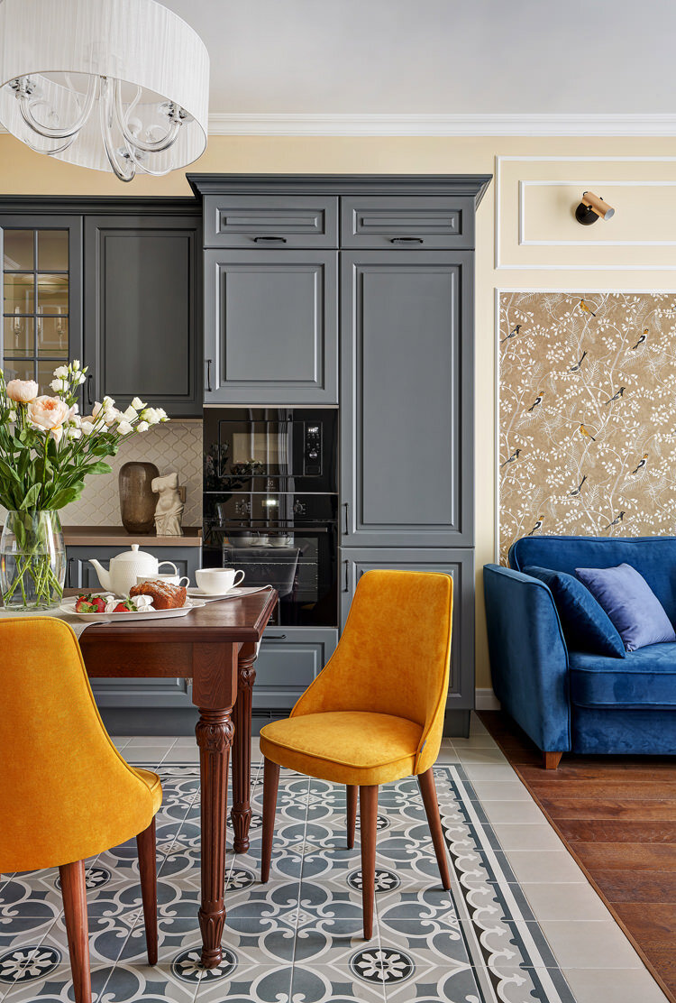 Кухня-гостиная в квартире в Москве по дизайну Юлии Бобровой. Кухонный гарнитур – Кухни Сити. Диван, обеденные стулья – Лавсит. Обеденный стол OneAndHome. Керамогранит Equipe Caprice. Обои KHROMA Kent.
