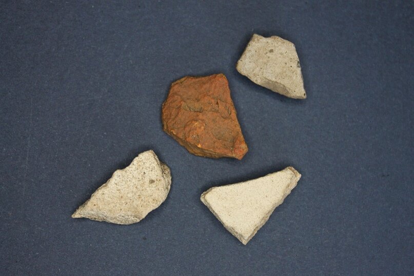 Осколки керамики из белой и серой глины. В центре для сравнения красноглиняный обломок.