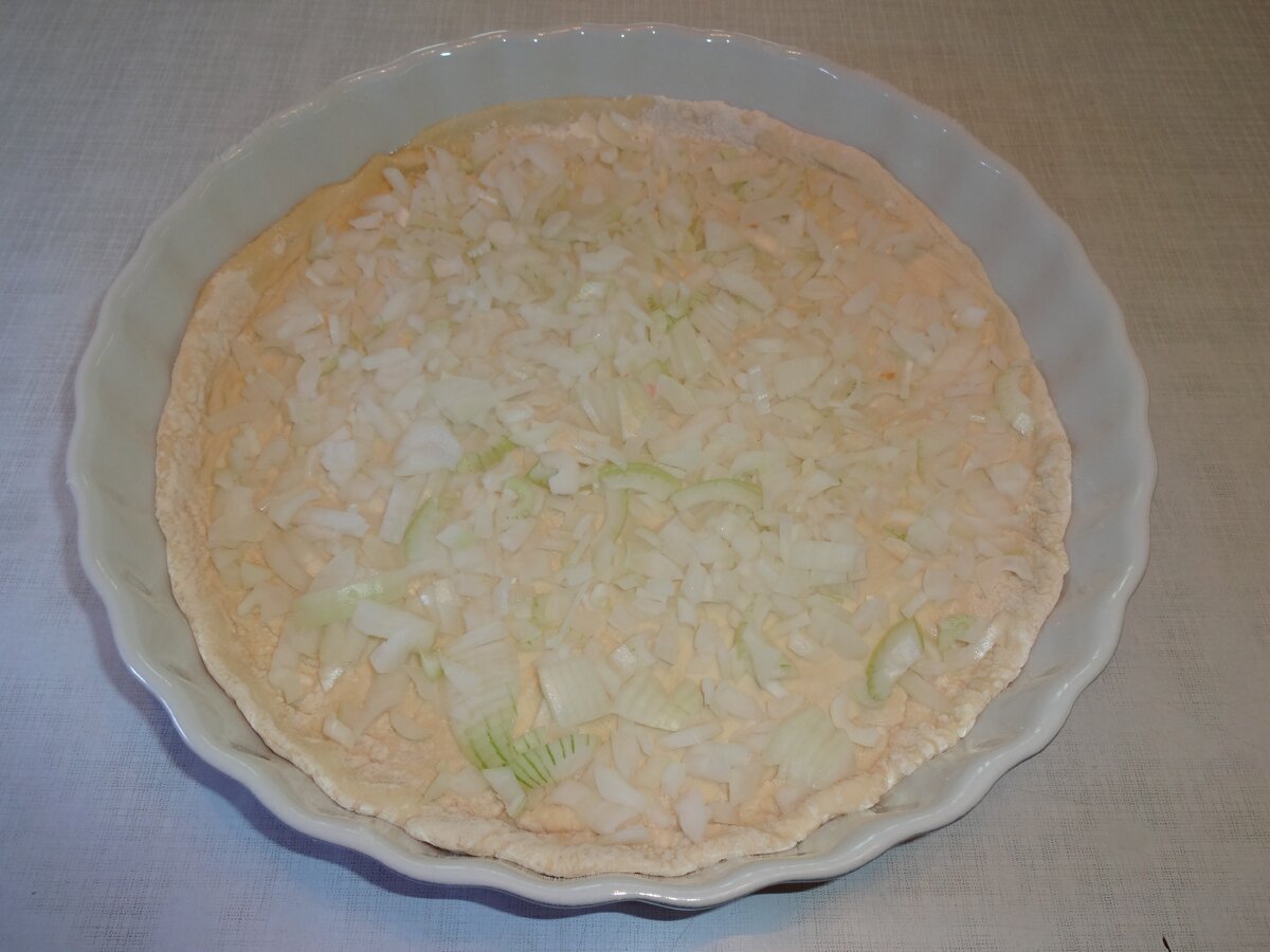 Выложите раскатанное тесто в форму, предварительно смазанную растительным маслом. Очень мелко покрошите репчатый лук. Выложите на тесто лук.
