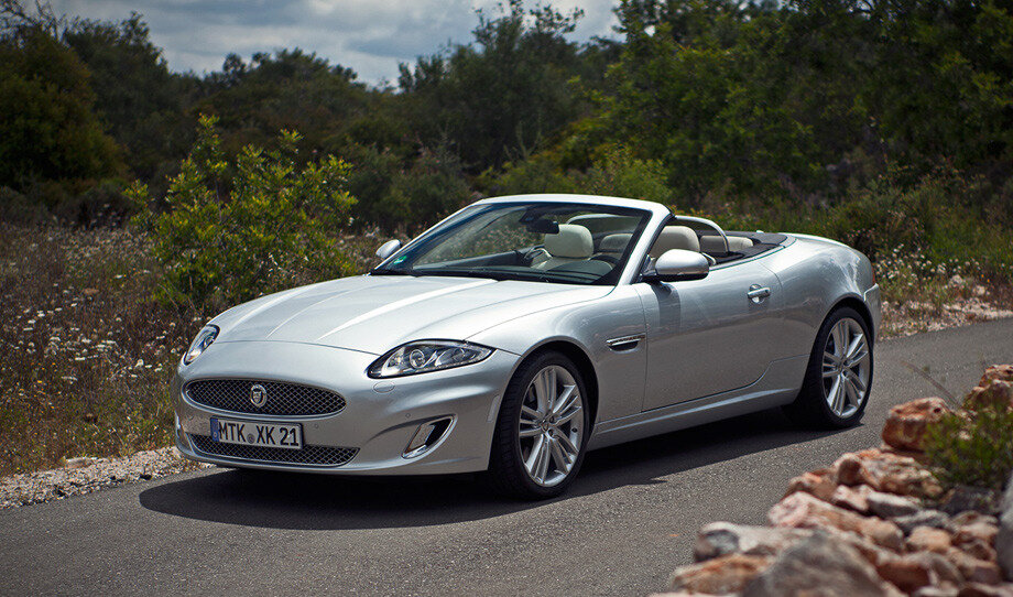 Ягуары и раньше были узнаваемы, но стиль, заданный седаном XJ, пришёлся машине впору. Опущенные вниз уголки фар делали предыдущий XK немного грустным, а теперь он стал агрессивнее. Настроение подчёркивают хромированные клыки воздуховодов. А вертикальные жабры на передних крыльях превратились в горизонтальные прорези а-ля BMW. 
Времени на долгие смотрины нет. Двигаю кресло так, чтобы доставать до педалей, осматриваюсь в салоне — тут не так просто определить нововведения. Создатели, как и обещали, добавили салону рафинированности. Улучшились материалы отделки (в купе, кстати, теперь можно обтянуть потолок кожей), приборы стали лучше читаться. Но с дисплеем на центральной консоли вышел казус. Графику-то ему подтянули до приличного уровня, а вот пластиковую рамку поменять не удосужились. Так что часть картинки по-прежнему уходит за обрез. Всё остальное — на привычных местах.