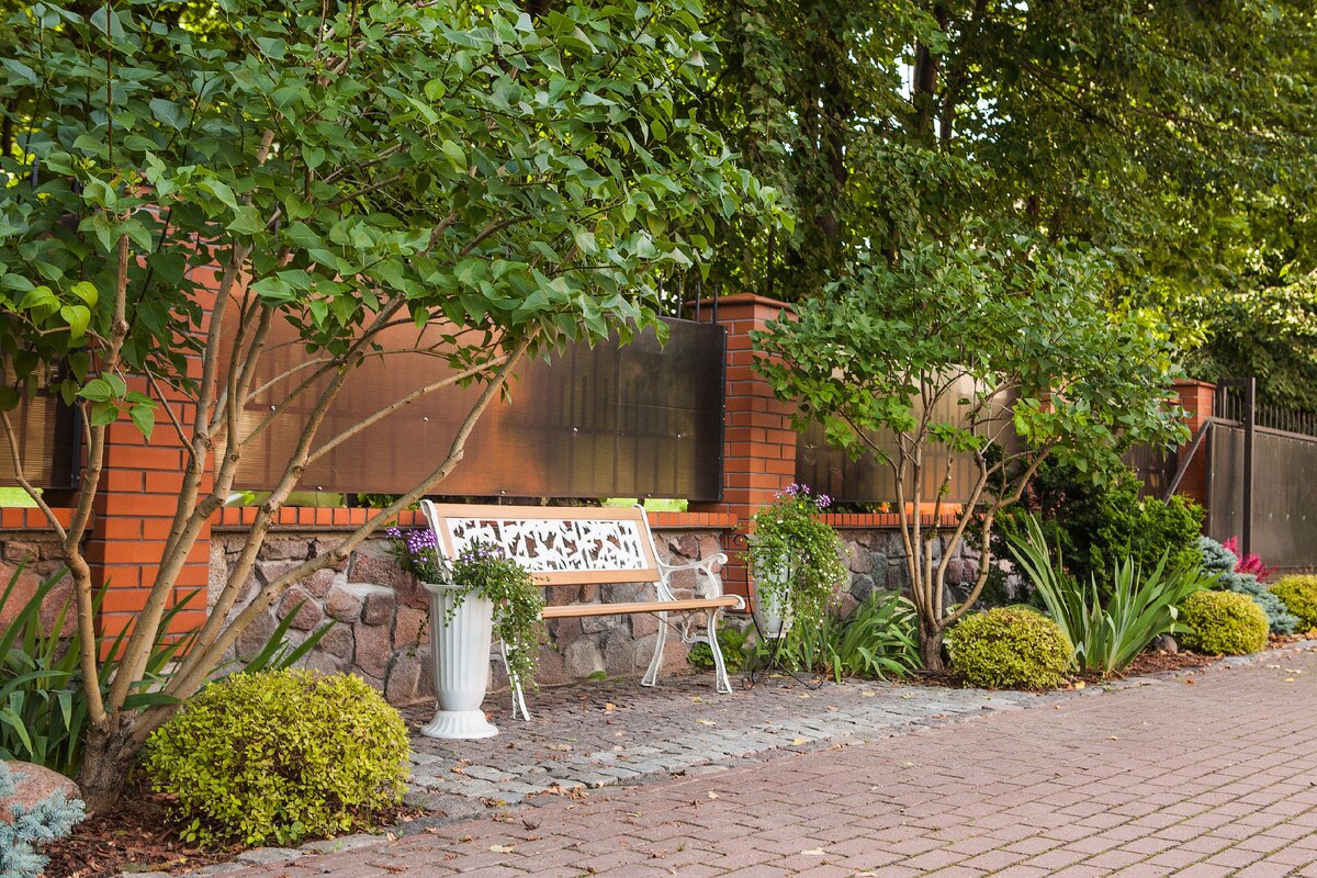 Зону отдыха у входа на участок украшает симметричная композиция из кустов сирени, спиреи Голдфлейм, ирисов, гортензии и хвойников.