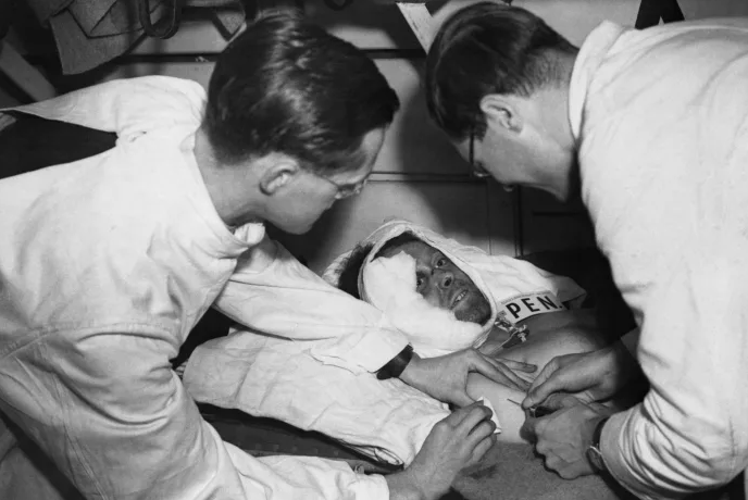 Травмированный ждет, пока медик введет пенициллин в рамках подготовки к операции в больничном поезде, направляющемся на станцию ​​в Англии.  Ранен во время атаки на позицию в Нормандии.