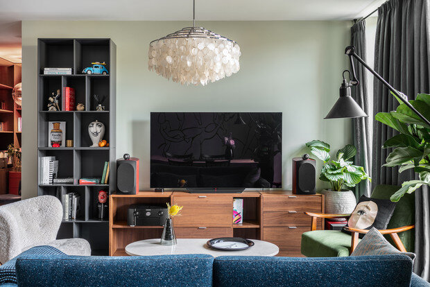 Гостиная с зоной «домашнего кинотеатра». Диван и зеленое кресло, Roche Bobois. Мохнатое кресло Little Petra, &Tradition. Журнальный столик September, Menu. Комод и книжные полки, BoConcept. Люстра, Verpan. Настенный светильник DCW Lampe, Gras. Декор, Tom Dixon, Fornasetti, Rosenthal.
