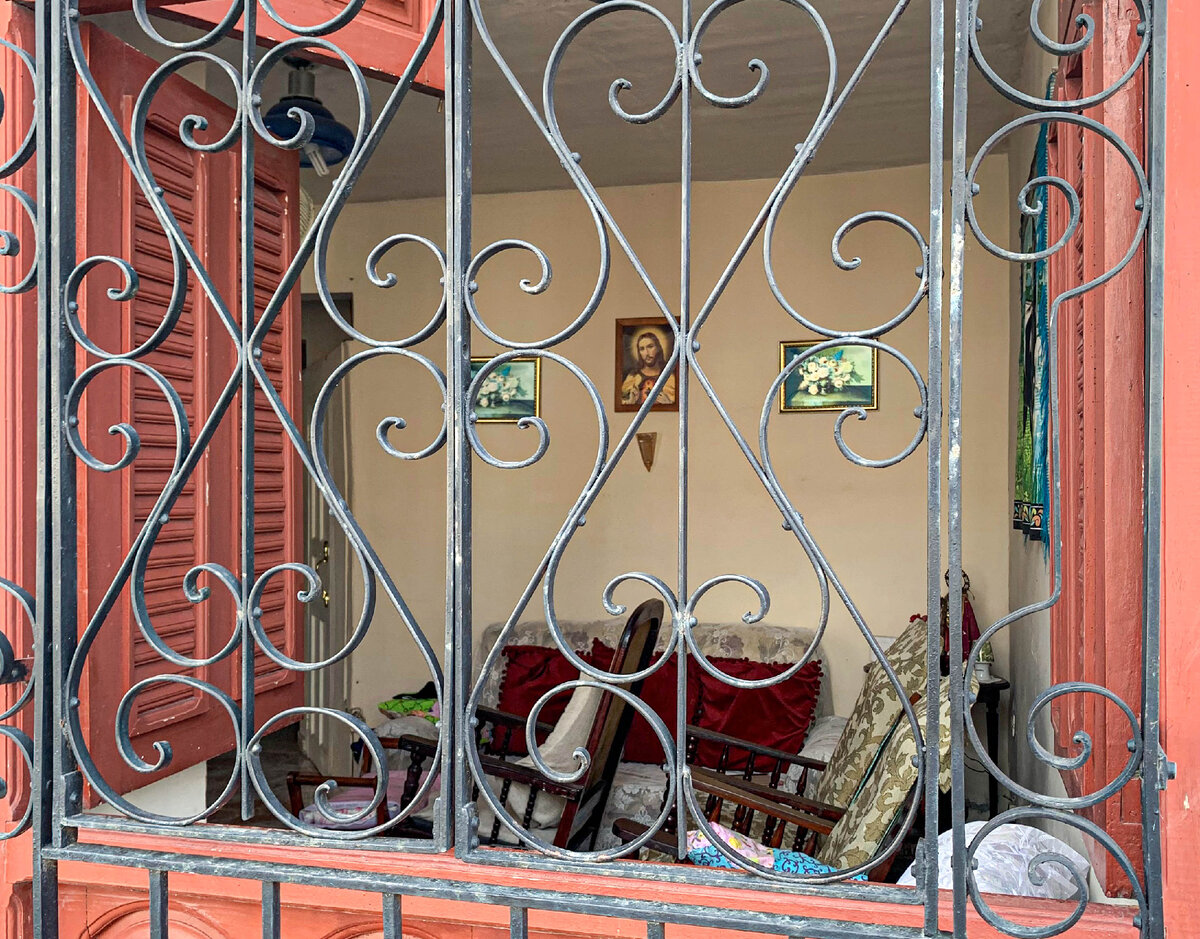 Обычное окно жилого дома на первом этаже. Стекло отсутствует, зато есть деревянные ставни и железная решетка