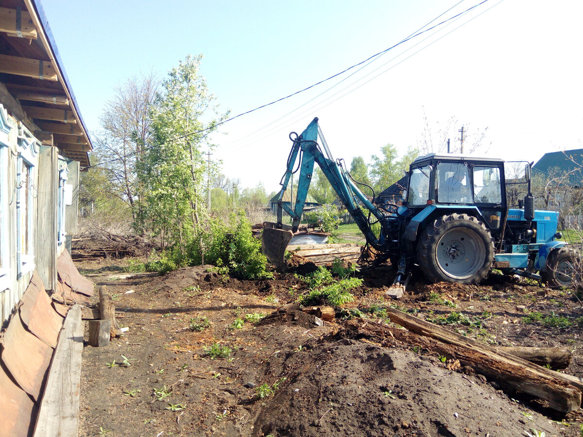 Трактор роет траншею и ревизионный колодец для водопровода.