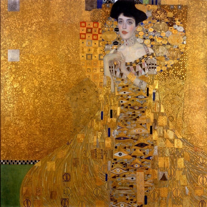 "Золотая Адель"
1907 г.
Густав Климт
Новая галерея, Нью-Йорк.

Существует легенда, согласно которой Фердинанд Блох-Бауэр заказал Густаву Климту портрет своей жены Адель, узнав об их романе. Оскорбленный и униженный мужчина придумал идеальный план мести неверной супруге и ее любовнику. Он пообещал художнику астрономическую сумму за уникальное полотно, во время работы над которым Климту приходилось бы проводить вместе с Адель так много времени, что вскоре она ему бы просто опротивела. Блох-Бауэр был наслышан о многочисленных любовницах художника и о том, что ни одна из них не задерживалась рядом с Климтом надолго. В итоге «Портрет Адели Блох-Бауэр» стал не только выгодным капиталовложением, но и прекрасным способом отомстить жене, которая вынуждена была каждый день наблюдать, как угасает страсть ее любовника.

Когда в 1938 году Германия вторглась в Австрию, практически всем имуществом семьи Блох-Бауэр завладели нацисты. В годы Второй Мировой портрет Адели скрывали от публики из-за явного еврейского происхождения модели, но после войны она заняла место в Галерее Бельведер. Единственная оставшаяся в живых представительница семьи Блох-Бауэр, племянница Фердинанда и Адели Мария Альтман, сбежавшая от преследования нацистов и ставшая гражданкой США, лишь в 1998 году узнала, что по завещанию дяди именно она является владелицей портрета. Так началась 8-летняя судебная волокита, ставшая причиной международного скандала. Но, в конце концов, Марии Альтман удалось вернуть себе и «Золотую Адель», и другие картины Климта, завещанные Фердинандом. Весной 2015 года на экраны вышел фильм «Женщина в золотом» с Хелен Миррен и Райаном Рейнольдсом в главных ролях, повествующий о борьбе Марии Альтман и ее адвоката с австрийскими властями. 

Портрет Адели Блох-Бауэр можно, пожалуй, назвать квинтэссенцией всего «Золотого периода» творчества Климта. В частности, это касается обилия драгоценного материала, который художник использовал в этой работе (Климт декорировал свои картины настоящим сусальным золотом). Тем не менее, полотно не выглядит вычурным или аляповатым. Обилие золота удивительным образом не создает ощущения богатства и роскоши, оно кажется лишь естественным обрамлением для красивой женщины, лицо и руки которой как будто выхвачены светом из общей картины. Климт написал портрет Адели на пике своей карьеры, использовав техники и приемы, которые позволяют безошибочно определить авторство любой из его зрелых работ. Здесь есть и отсылки к египетскому и византийскому искусству, и разнообразие орнаментов, мастерски вписанных в пространство картины и облачение героини, и, конечно же, неуловимая чувственная аура, окружающая «Золотую Адель».

