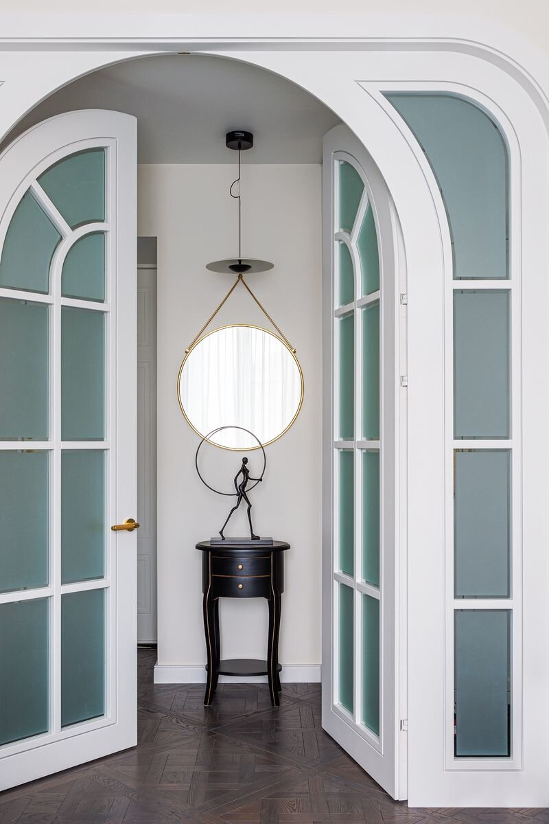 Вид из гостиной на зону прихожей. Распашные двери с фрамугами выполнены на заказ в столярной мастерской «Парадизайн хоум». Зеркало, Eicholtz. Светильник, Marset.