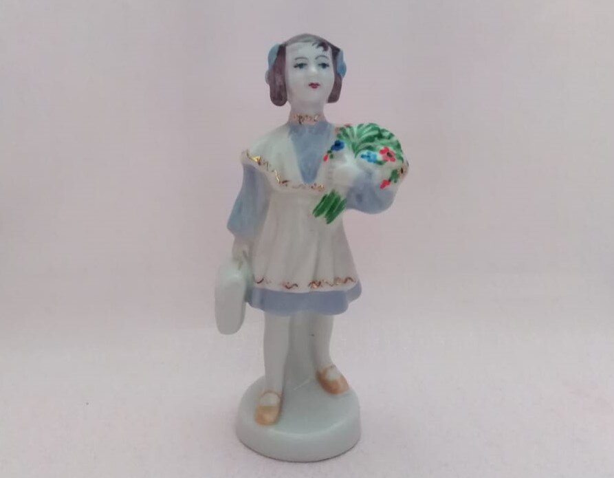 Вспомните советские школы. А ту школьную форму? Как же я ненавидела это коричневое платье. Ткань, которая блестела, если неправильно погладить, а как гладить то не хотелось! А черный фартук? Потому что белый, можно было надевать только по праздникам. И портфели мы уже все давно забыли, рюкзаки плотно вошли не только в жизнь школьников, но во взрослую. 
Похоже, что моя ученица идет в школу либо 1 сентября, либо уже на последний звонок - с букетом цветов и в белом фартуке. Таких школьниц делали на многих фарфоровых заводах, они отличались по форме исполнения, но все были яркими представителями советской школы. Моя девочка сделана на Барановском Фарфоровом заводе, высота 14 см.