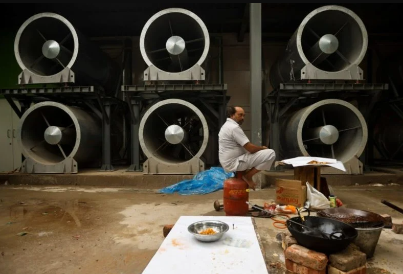 Мужчина сидит рядом с башней от смога в Нью-Дели