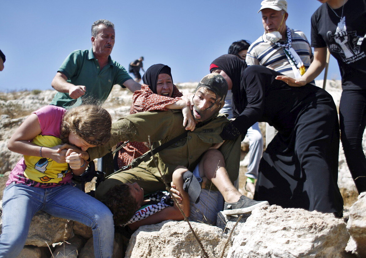 Ahed (left) is seen biting an Israeli soldier who is wrestling her 11-year-old brother to the ground. The soldier was detaining the boy on suspicion of throwing stones. © Mohamad Torokman / Reuters