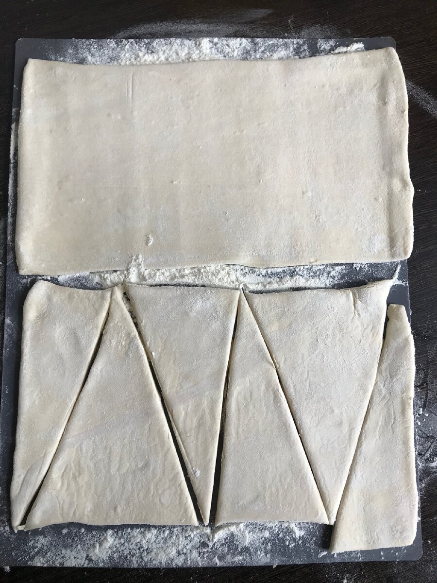 Готовое тесто размораживаем при комнатной температуре, выкладываем на посыпанную мукой поверхность, немного раскатываем. Толщина теста примерно 0,5 см. И нарезаем на треугольники 