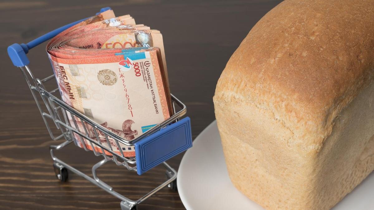    Пачка тенге лежит в миниатюрной корзине рядом с булкой хлеба:Getty Images/Yevgeniy Sambulov