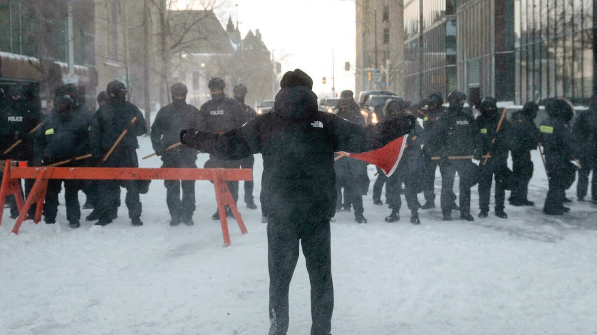 Протестующие держат флаг перед полицейской линией на Кент-стрит после того, как полиция очистила Веллингтон-стрит, ранее оккупированную "Конвоем свободы", в Оттаве, Канада, 19 февраля 2022 года. AFP - АНДРЕЙ ИВАНОВ 