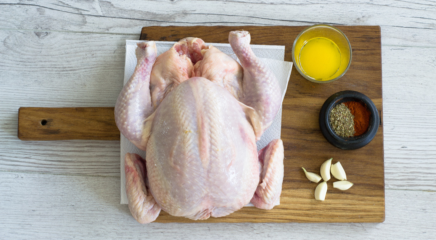 Подготовьте курицу для запекания в рукаве. Тушку вымойте, затем обсушите внутри и снаружи бумажными полотенцами. Орегано и паприку смешайте. Головку чеснока разберите на зубчики. Сливочное масло растопите.