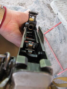 Вид на открытую штампованную ствольную коробку АК.Слева сверху и справа снизу от казённого среза ствола видны боевые упоры. Слева снизу — выступ, направляющий движение патрона, подаваемого из левого ряда магазина. Все они конструктивно выполнены в виде единой детали — вкладыша. Загибы в верхней части стенок ствольной коробки служат верхними направляющими, а приваренные к стенкам изнутри штампованные детали — нижними. В задней части ствольной коробки просматриваются детали УСМ и задний вкладыш, служащий для установки основания возвратной пружины.