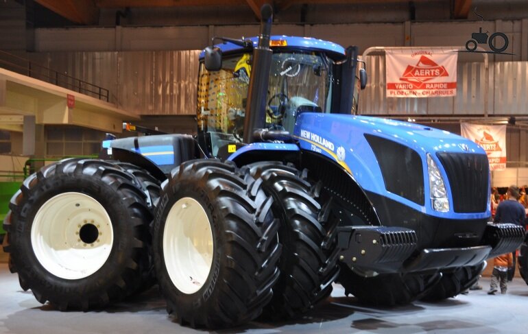 Под маркой New Holland (Нью Холланд) производятся различные сельхозмашины, линейка которых включает более 70 базовых моделей. Одним из востребованных видов самоходной техники этого бренда являются тракторы. Благодаря мощному тяговому механизму, высоким техническим показателям, работоспособности, продуктивности и функциональности, они нашли успешное применение в широких отраслях деятельности. Своё существование компания-производитель начала в 1895 г. с крохотной мастерской, основанной в городке New Holland (США, штат Пенсильвания). Небольшое предприятие сначала занималось только техническим ремонтом сельхозмашин, но вскоре наладило и их производство, тогда и открылся полноценный завод. В настоящее время оно превратилось в крупнейший международный концерн с мощными производственными и научно-исследовательскими подразделениями, открытыми на территории 17 стран, а так же сетью дилерских и специализированных сервисных центров во всех регионах мира.

Технические особенности и применение
Минитракторы и тракторы модельного ряда New Holland производятся по самым актуальным и передовым технологиям. От сельхозмашин других марок их отличает качество сборки, большая функциональность, возможность работать практически в любых климатических условиях. Они проходят всесторонние испытания, поэтому отвечают высоким стандартам качества. Выпускаемые концерном модели обладают рядом отличительных характеристик.

Весь модельный ряд имеет:

узкую вытянутую форму капота, который слегка наклонён для улучшения обзорности и неизменно выкрашен в яркий синий цвет;
удлинённую базу ходовой части, что обеспечивает оптимальный баланс при выполнении сложных работ;
широкие пневматические колёса с крупным «ёлочным» протектором, что гарантирует повышенную проходимость.
Хотя сельхозтехника данного бренда обладает внушительными габаритами, но это не мешает оператору легко управлять ею. При всей своей мощи, она издаёт мало шума и не загрязняет окружающую среду вредными выхлопными газами.

Тракторы модельного ряда Нью Холланд широко применяются не только в таких областях сельского хозяйства, как растениеводство, животноводство и земледелие с целью обработки поля и проведения рядового сева, подкормки, опрыскивания культур. Для выполнения разноплановых работ их используют строительные компании, а так же дорожные, коммунальные и лесозаготовительные предприятия. 
