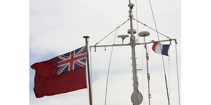Британское судно в порту Тулон (Франция), На кормовом флагштоке британский флаг, а под краспицей "гостевой флаг" Франции. Хорошо видно, что гостевой флаг гораздо меньше кормового.