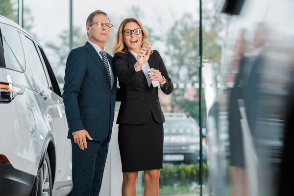 Это то, что нам надо!                                                                                                                            Изображение с сайта: https://ru.depositphotos.com/category/nature.html">Business woman with smartphone pointing away while looking for new automobile together with businessman in dealership salon - null</a>